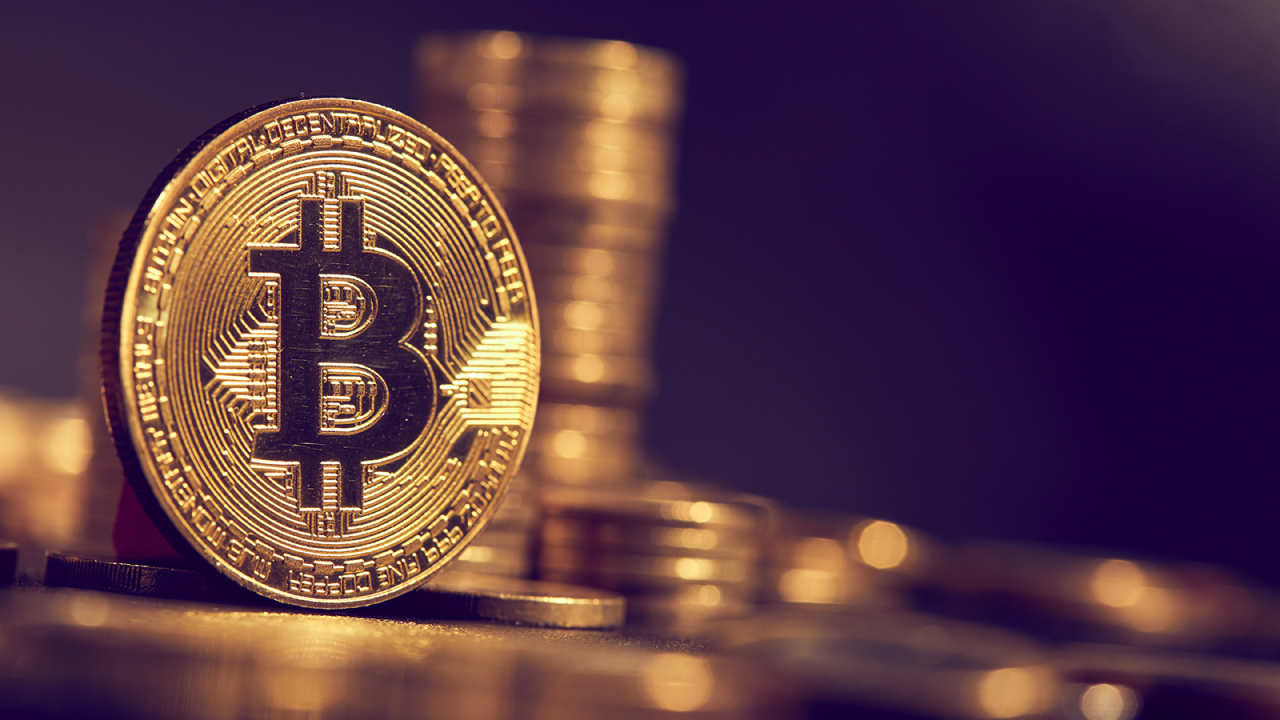 Closeup of a gold Bitcoin with blurred piles of Bitcoins in the background.